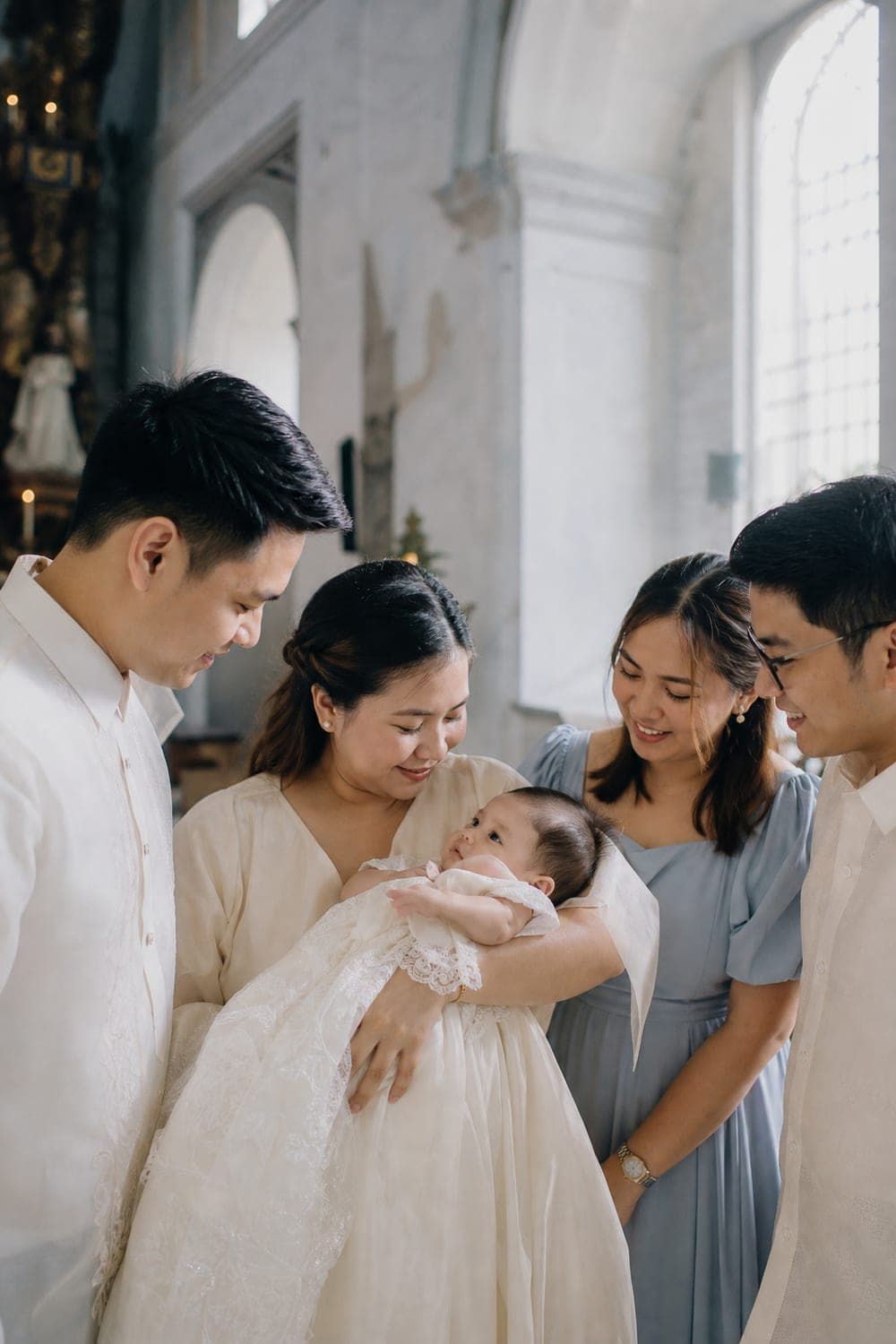 Baby in a christening gown held by her mother with the godparents