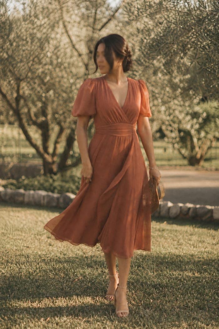 Guest in a terracotta chiffon midi dress on a lawn